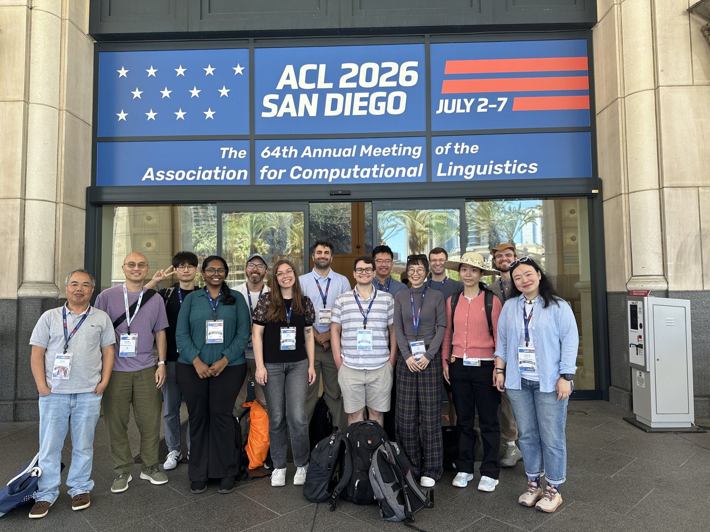 The full Brandeis cohort — about a dozen students and faculty — posing together under the ACL 2026 San Diego banner at the venue entrance.