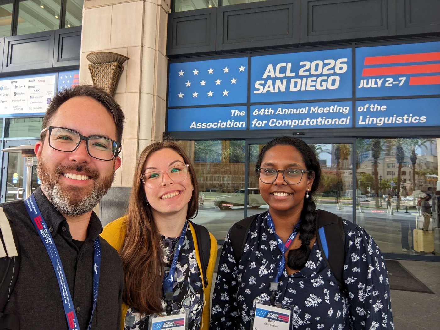 Selfie of Anna, Marc, and Edith smiling in front of the ACL 2026 San Diego banner at the venue entrance.