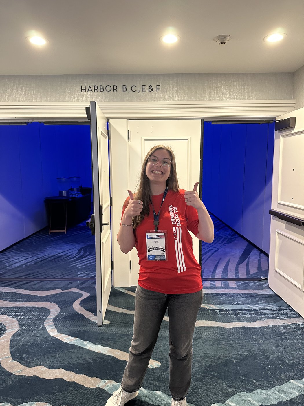 Anna in a red volunteer shirt standing by the entrance to the Harbor orals room.