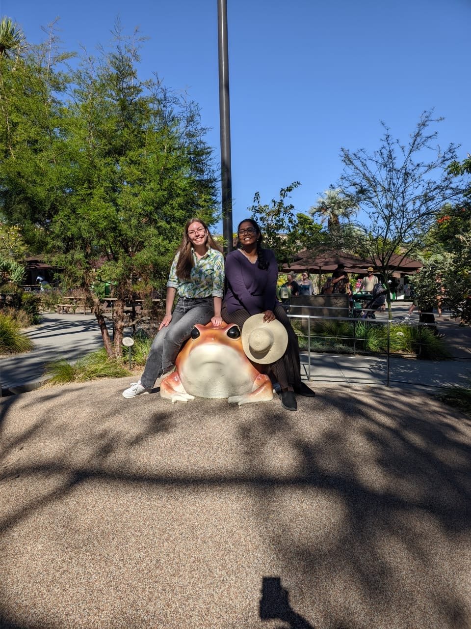Two friends perched on a bronze animal statue at the zoo.