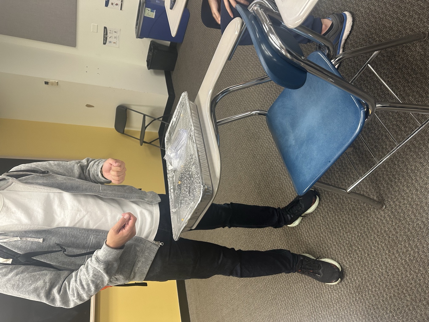 A foil tray of BBQ brisket balanced on a classroom desk.