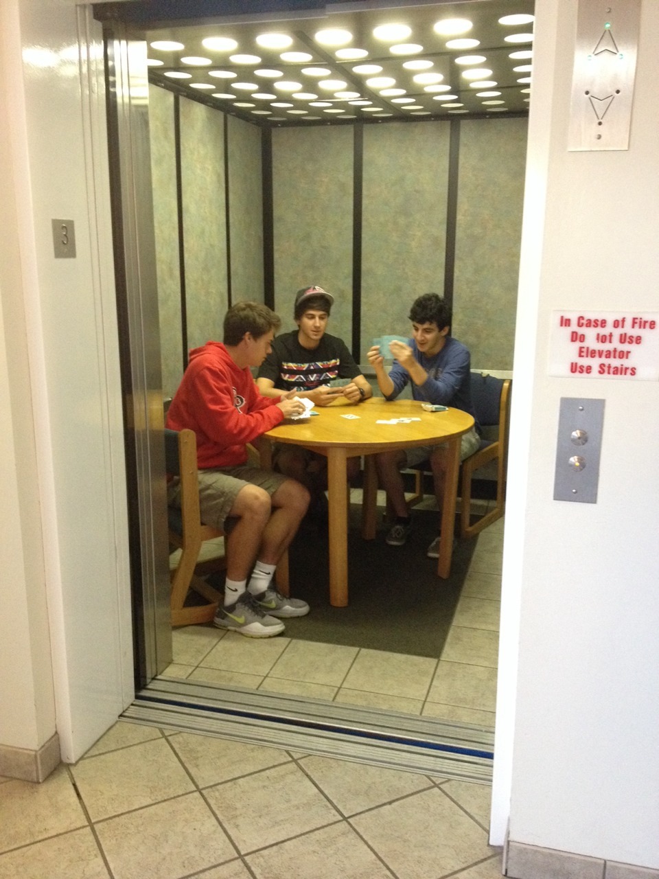 A group of friends playing a card game inside a dorm elevator.