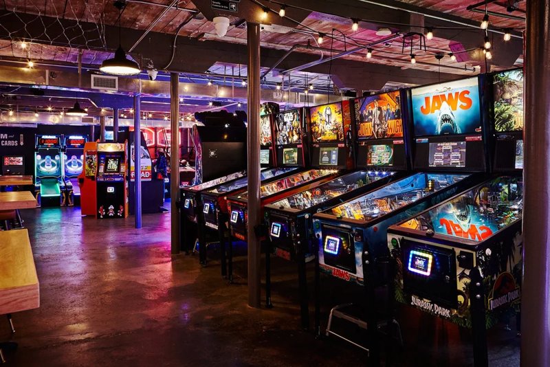 The arcade room at Foo Bar in Charlotte: rows of lit-up pinball machines under string lights.