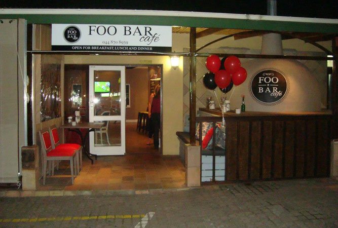 The front of Foo Bar Cafe in George at night, with red chairs and balloons by the door.