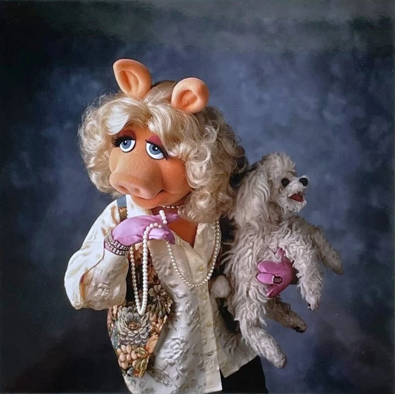 Miss Piggy in pearls and a floral vest, holding Foo-Foo, her small white poodle.