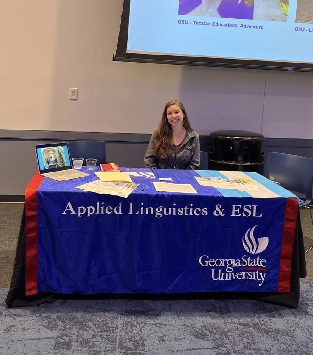 Anna seated behind a Georgia State University 'Applied Linguistics & ESL' booth at the study abroad fair.