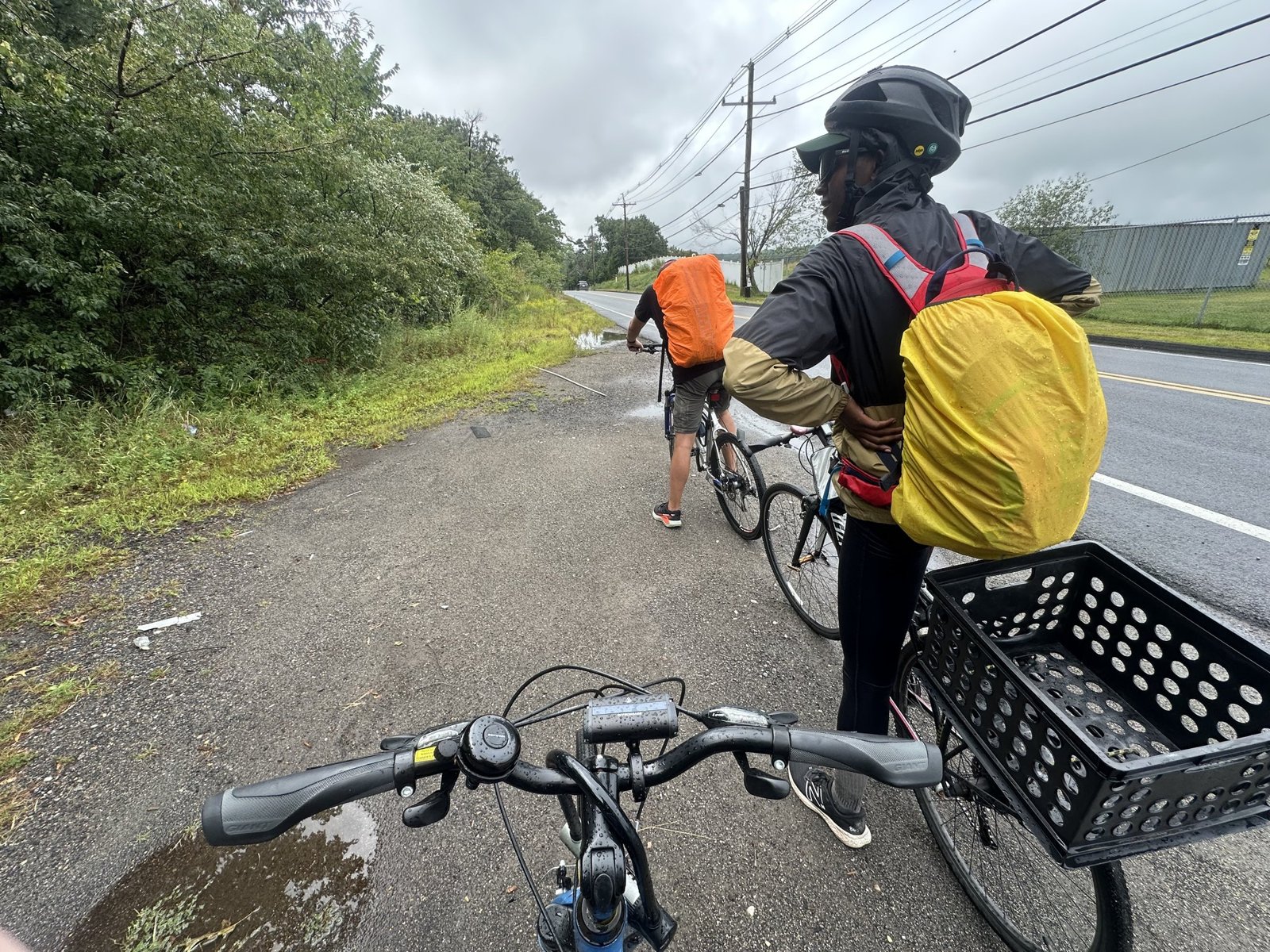 From behind handlebars: Marc and Sharde stopped on the shoulder of a road, backpacks in orange and yellow rain covers, checking a phone.