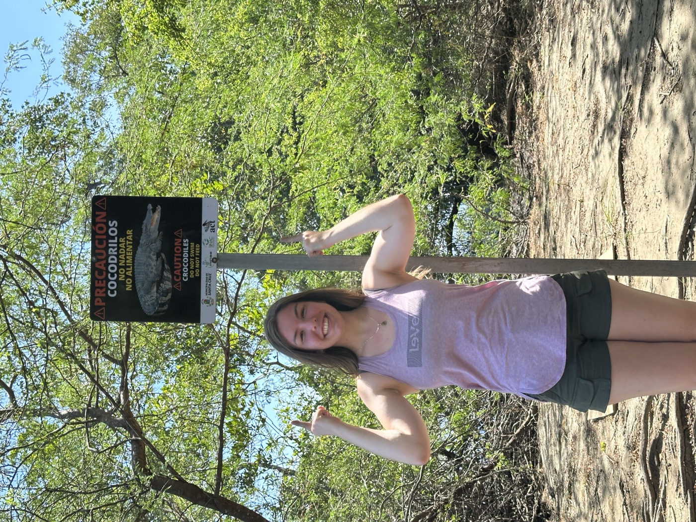 Anna giving thumbs up beneath a 'Caution: Crocodiles' sign.