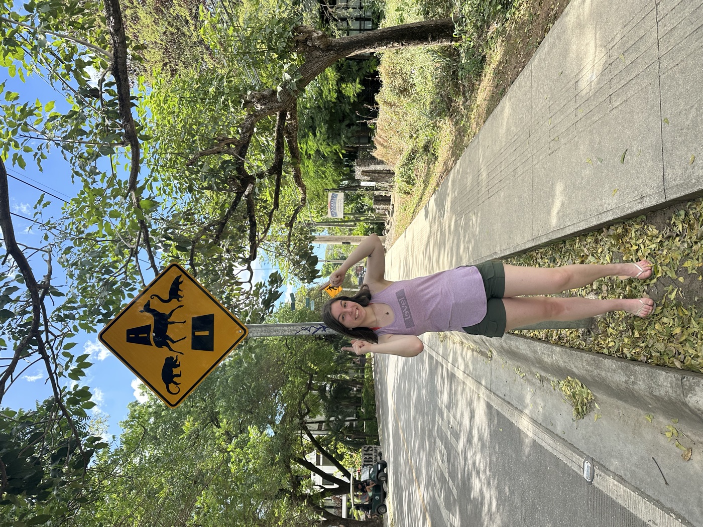 Anna pointing at a yellow sign showing a monkey, a deer, and a coati crossing a road.